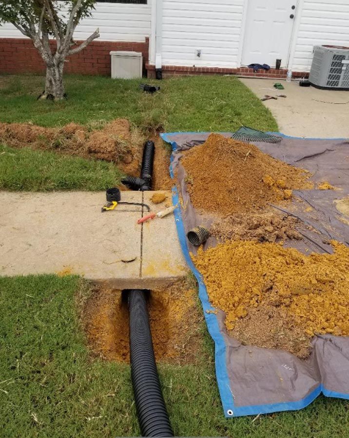 A drain pipe is being installed in a yard next to a house.