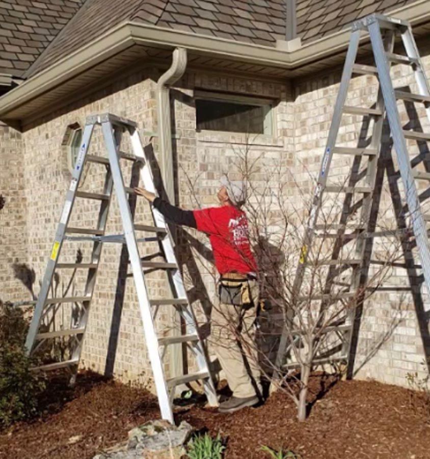 A man is standing on a ladder in front of a brick house