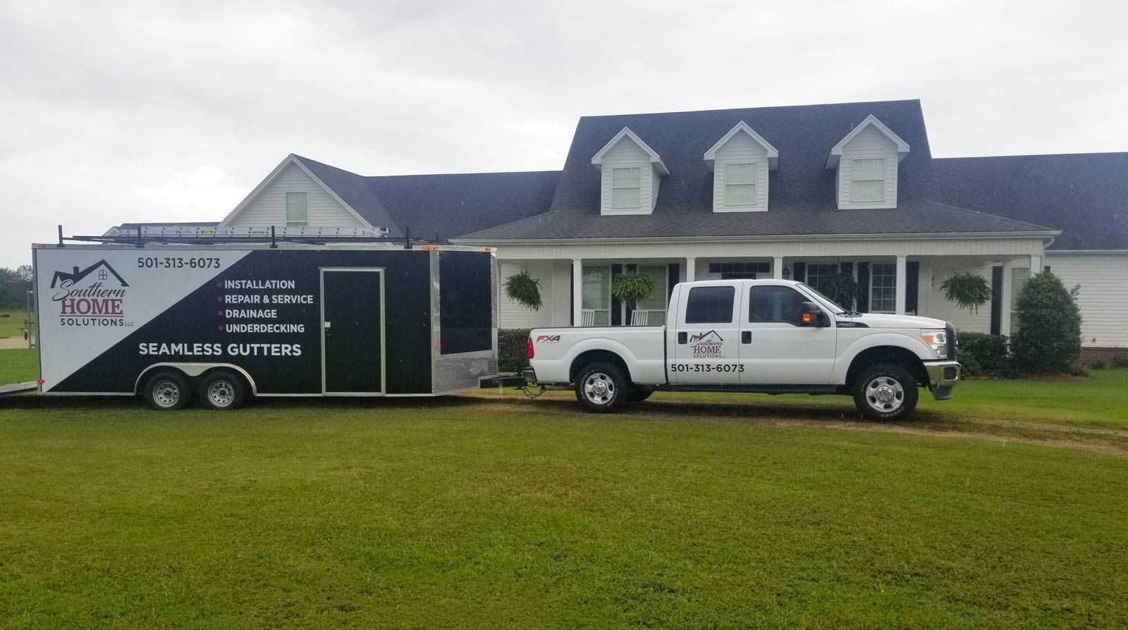 A white truck is parked in front of a house with a trailer attached to it.