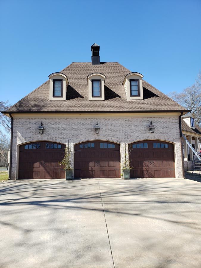 A large house with three garage doors and a chimney on the roof.