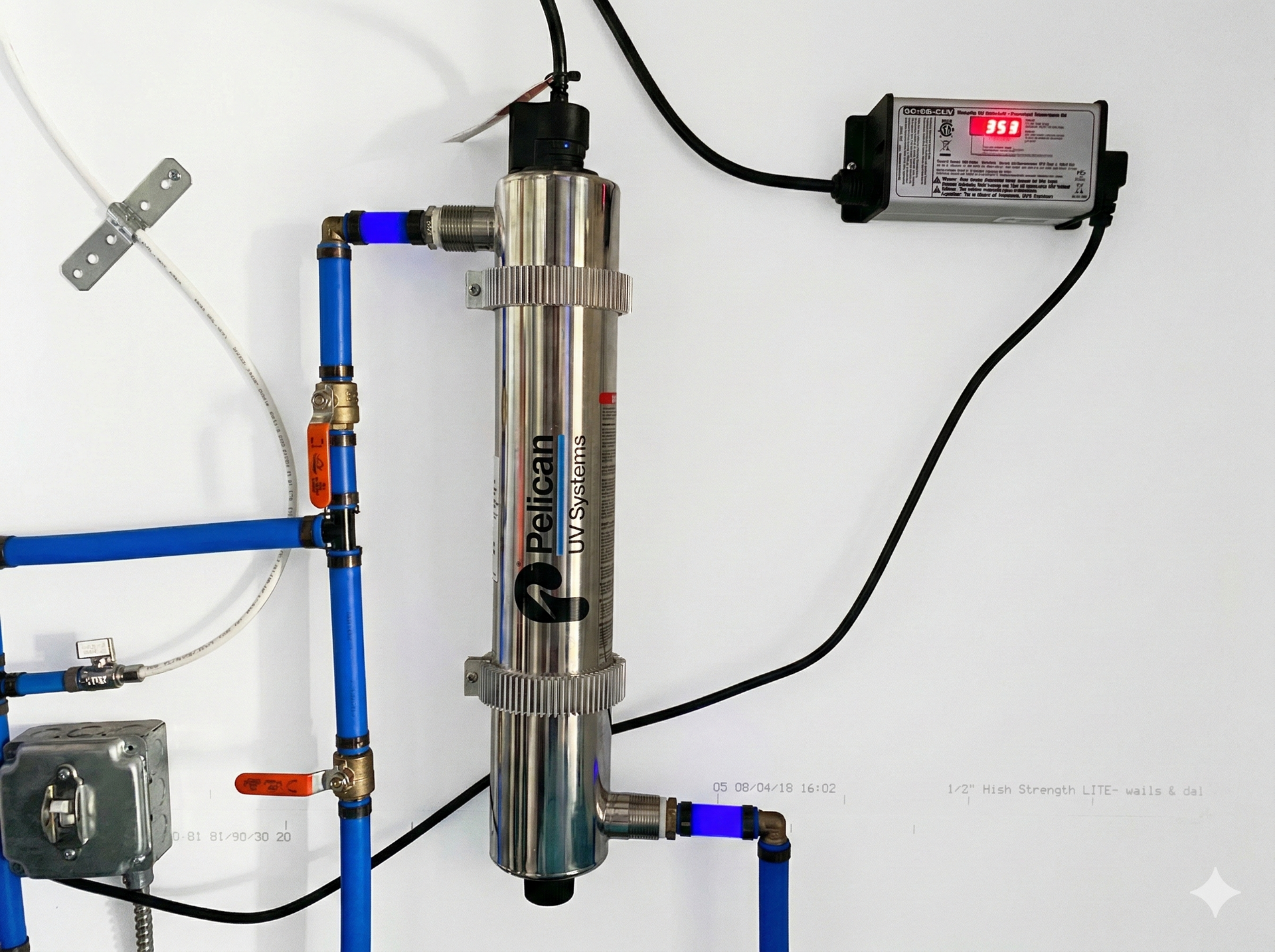 Ultraviolet water filtration system installed on a white wall, showing plumbing, Pelican brand filter, and power supply.