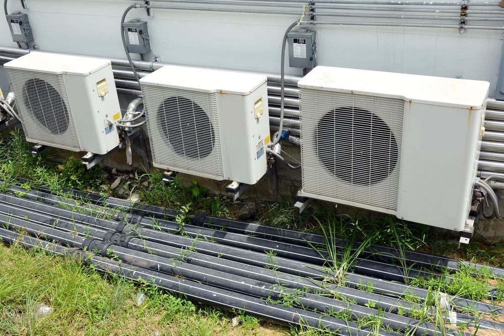 A Three White Air Conditioning Units Outside, With Black Pipes in the Grass — Escarpment Air in Nowra, NSW