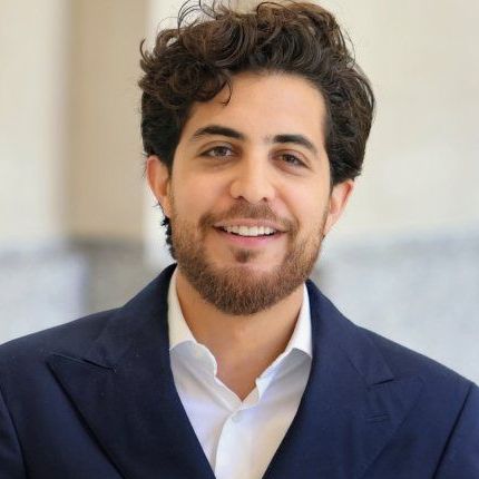 A man with a beard wearing a blue jacket and white shirt is smiling for the camera.
