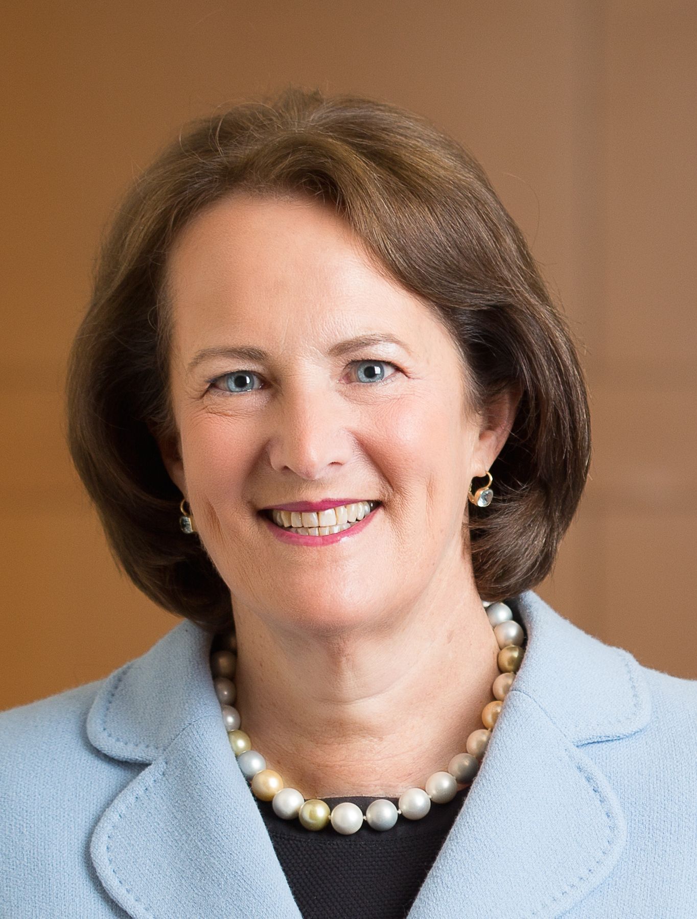 A woman wearing a blue jacket and a pearl necklace is smiling for the camera.