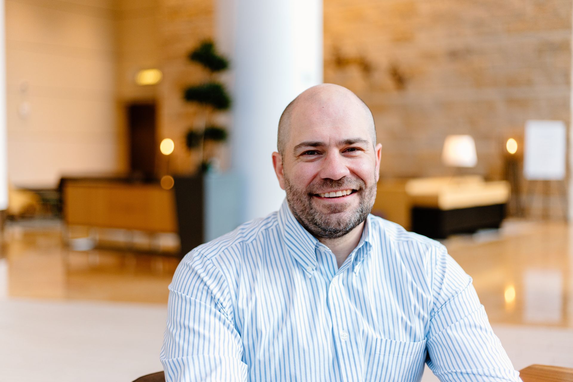 A bald man with a beard is smiling for the camera while sitting in a chair.