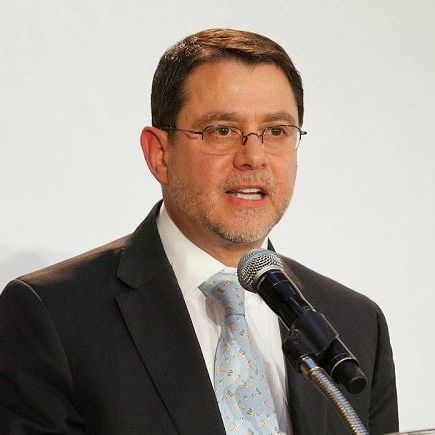 A man in a suit and tie is speaking into a microphone.
