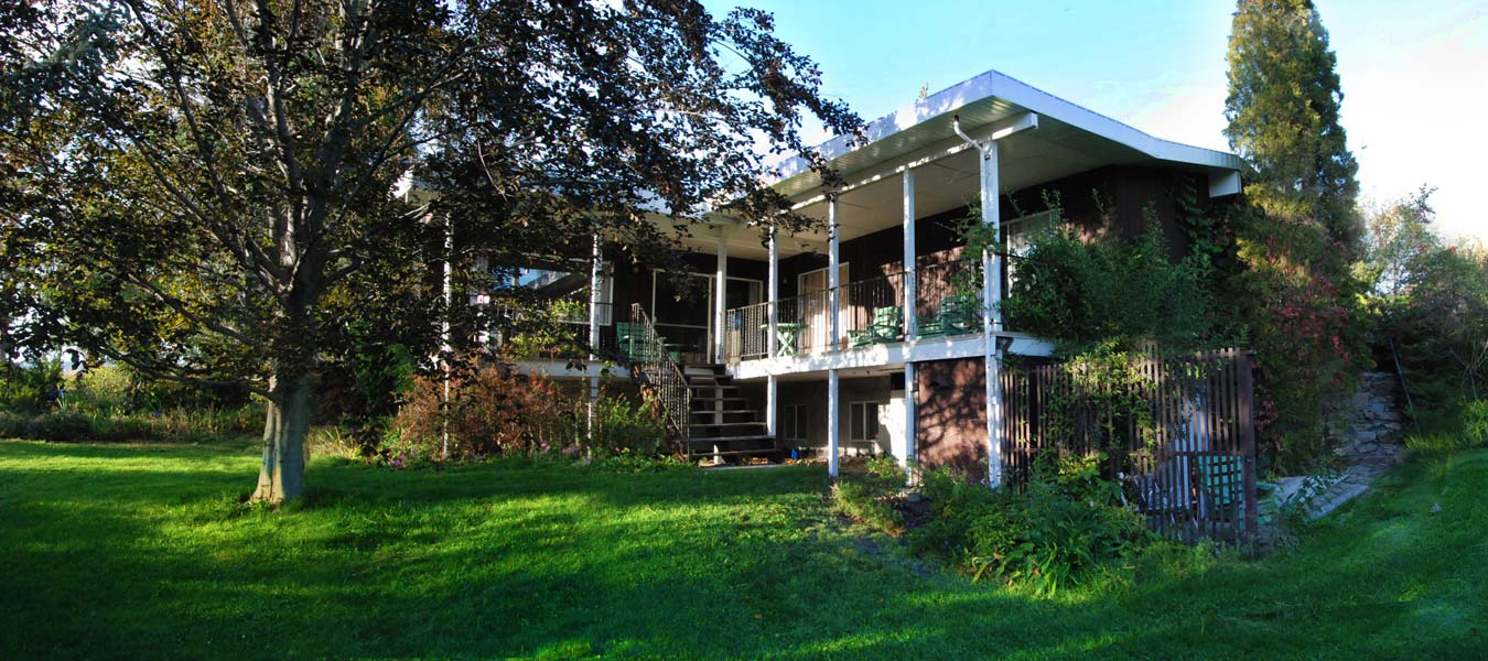 A large house with a large porch is surrounded by trees and grass.