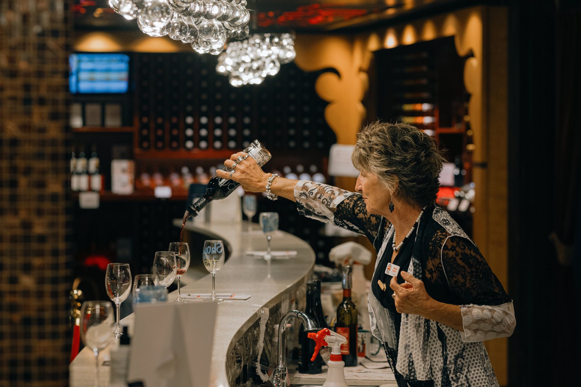 A woman is pouring wine into a glass at a bar.