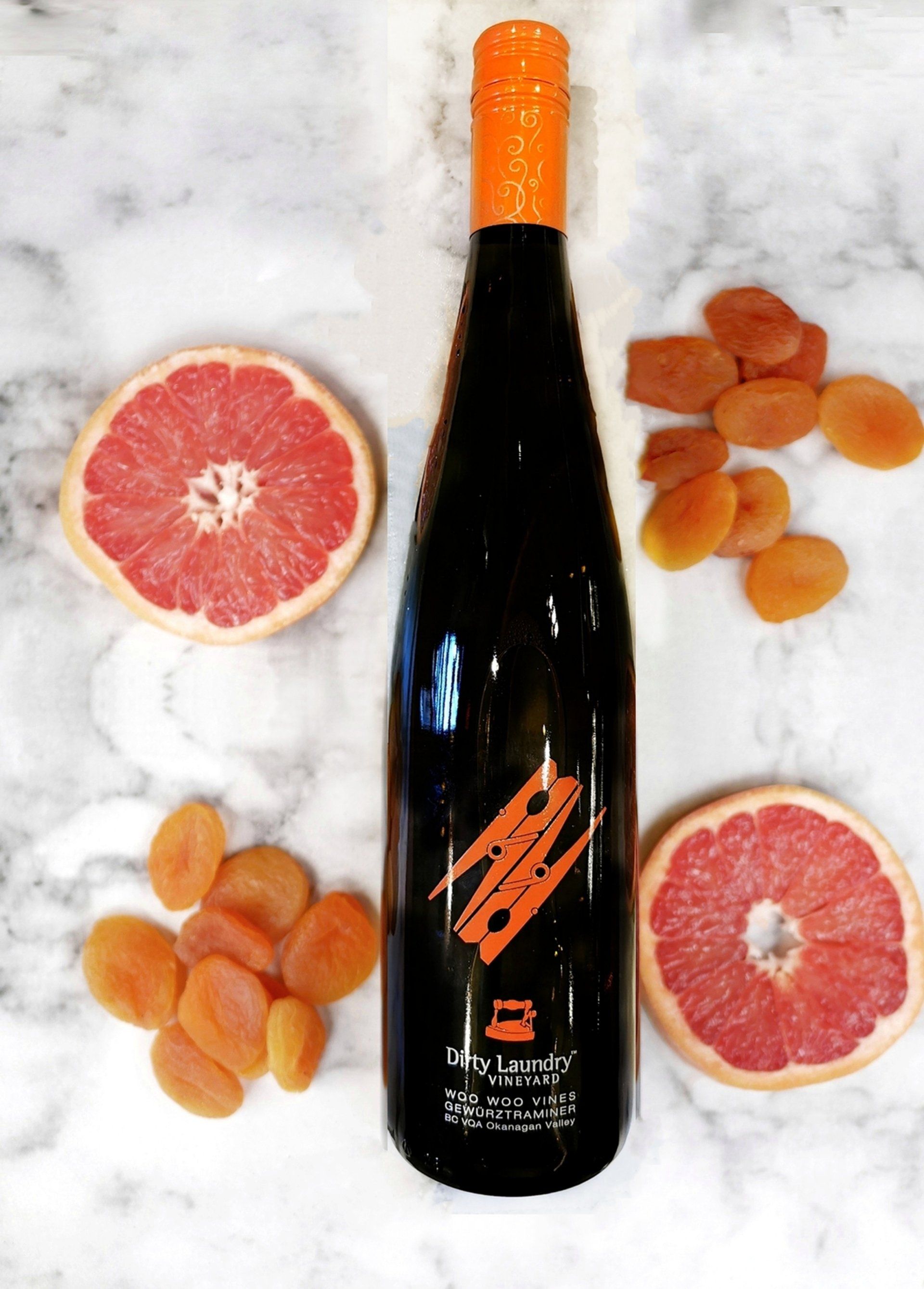 A bottle of wine is surrounded by grapefruit and apricots