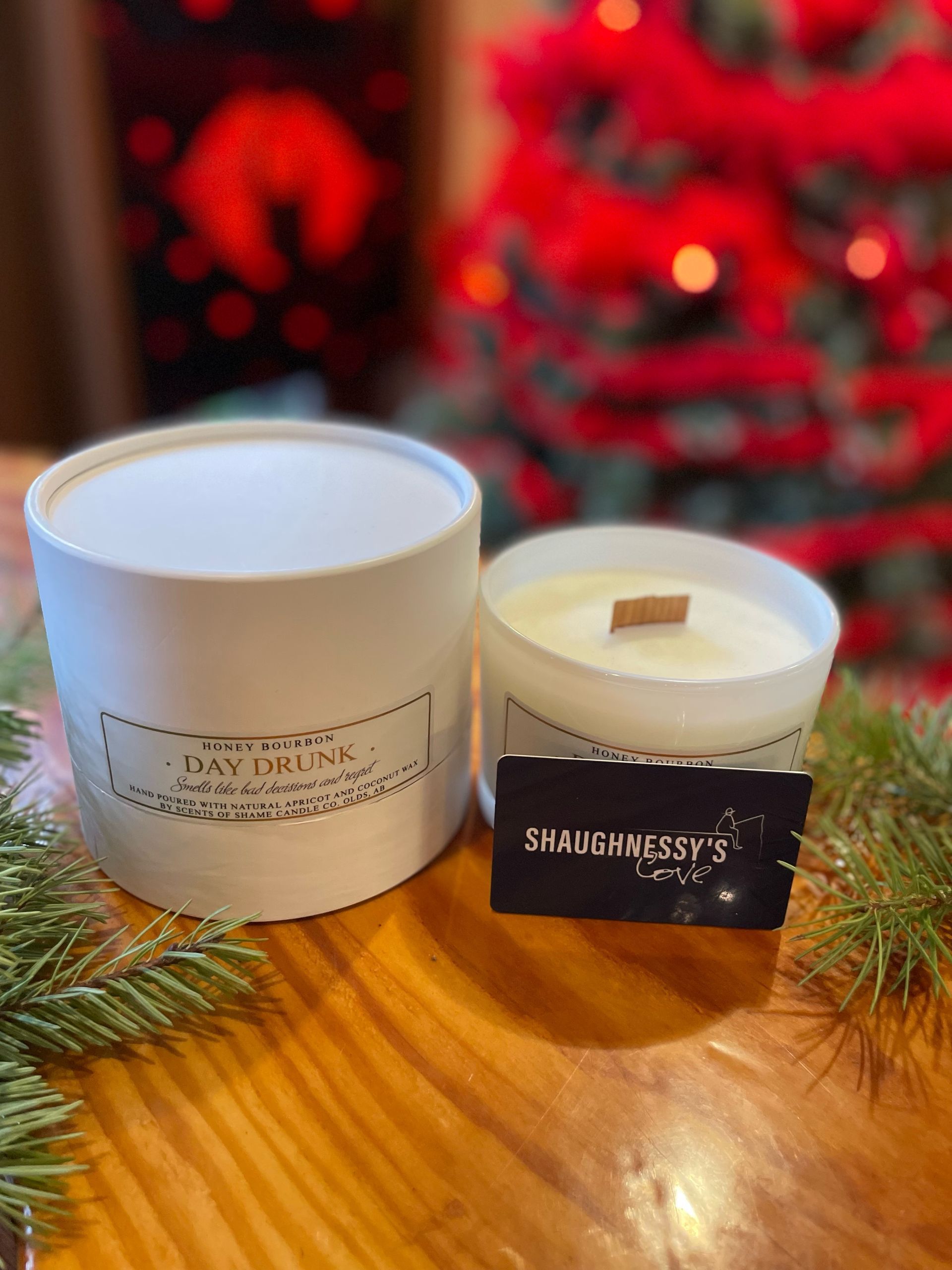 Two candles are sitting on a wooden table in front of a christmas tree.