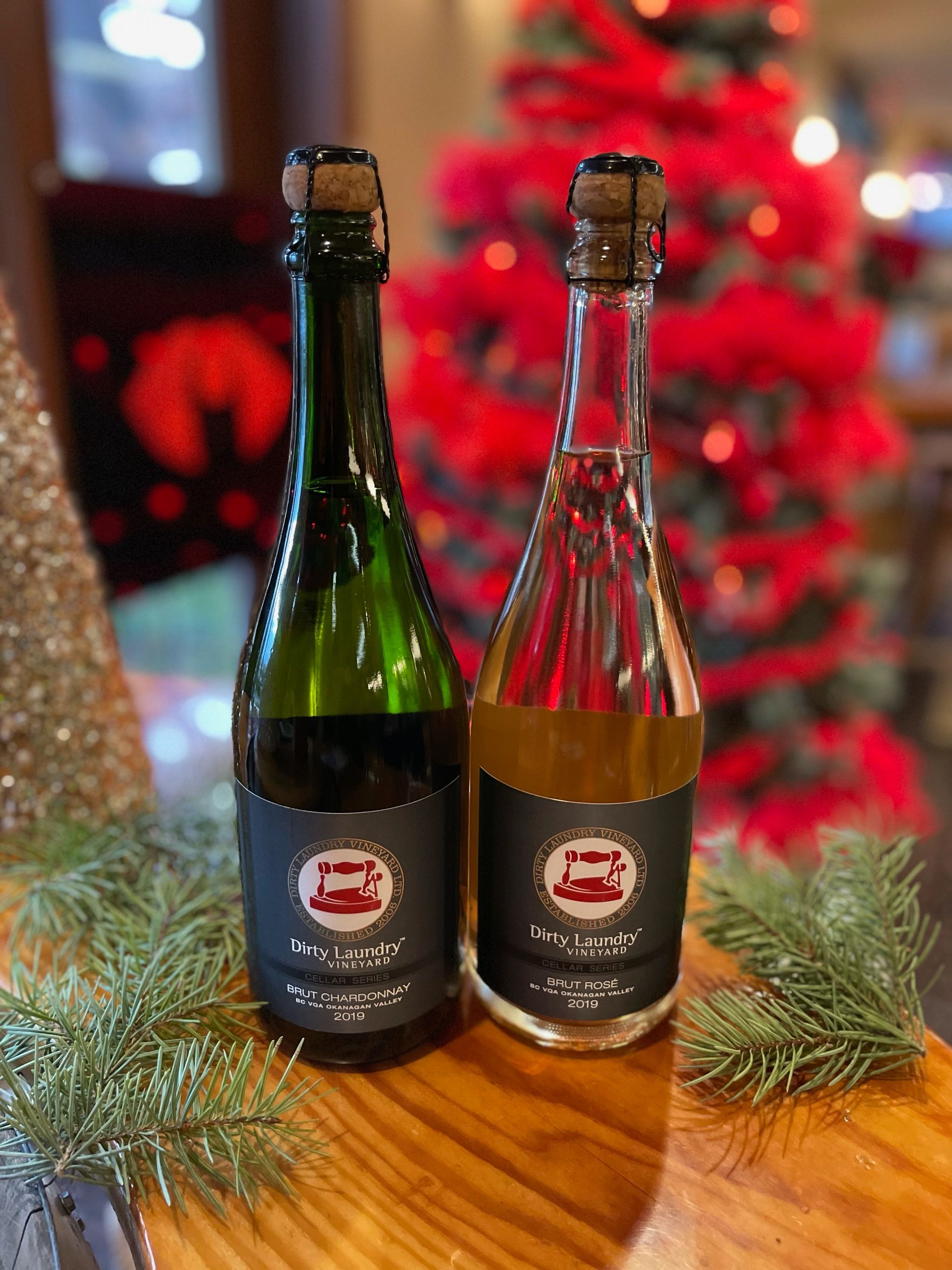 Two bottles of wine are sitting on a wooden table in front of a christmas tree.