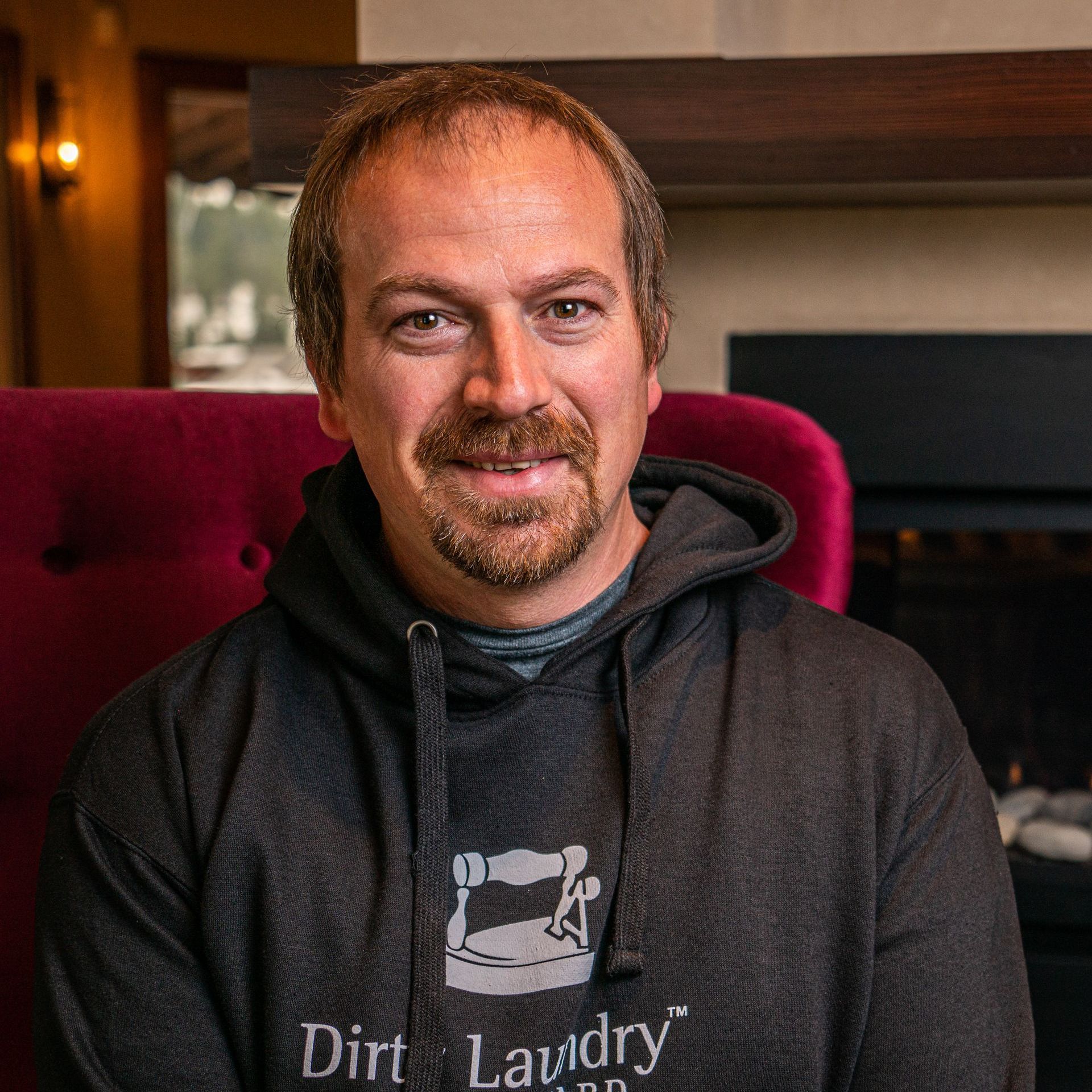 A man wearing a dirt laundry hoodie is sitting in a chair