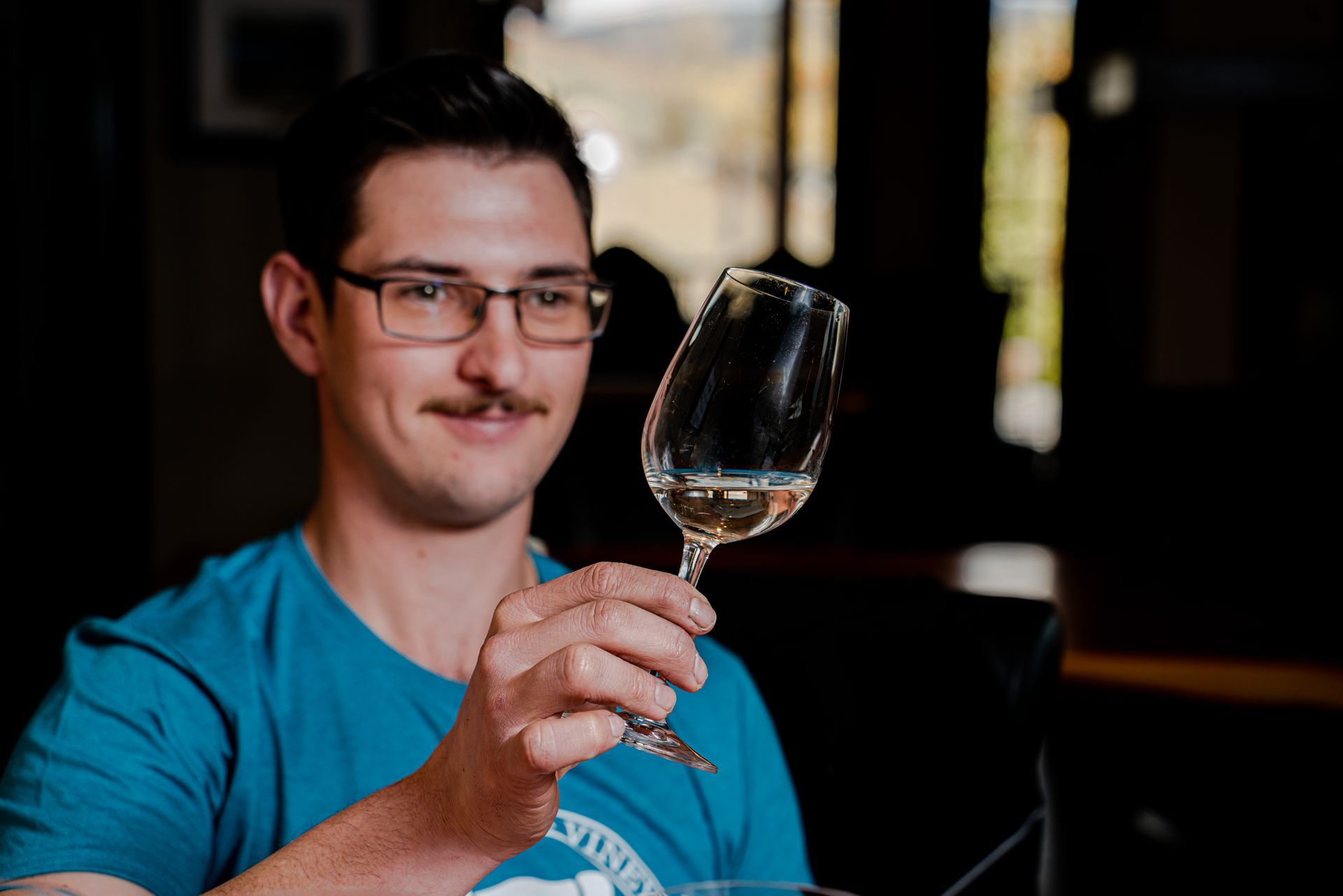 A man in a blue shirt is holding a glass of wine.