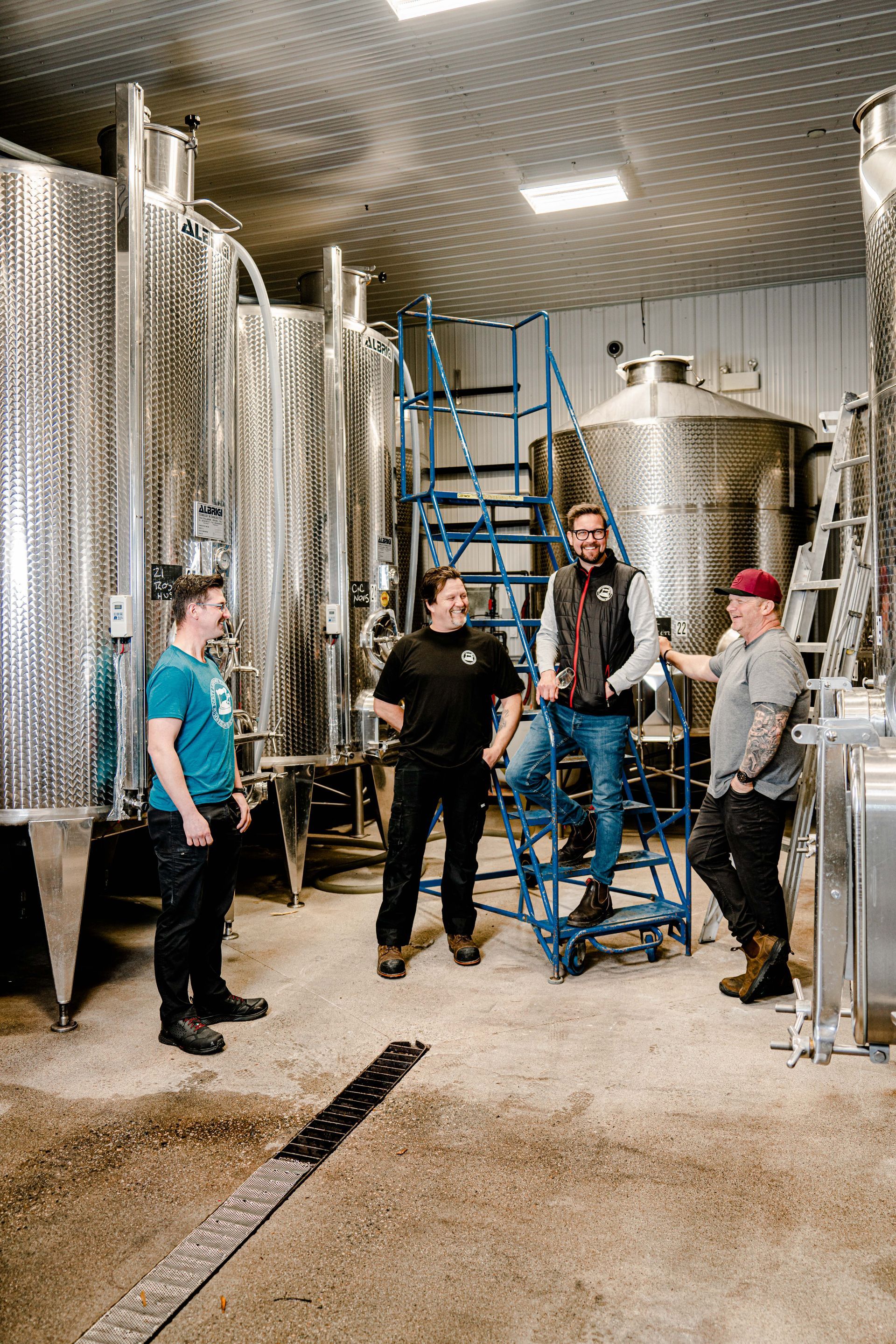 A group of men are standing in a room with stainless steel tanks.