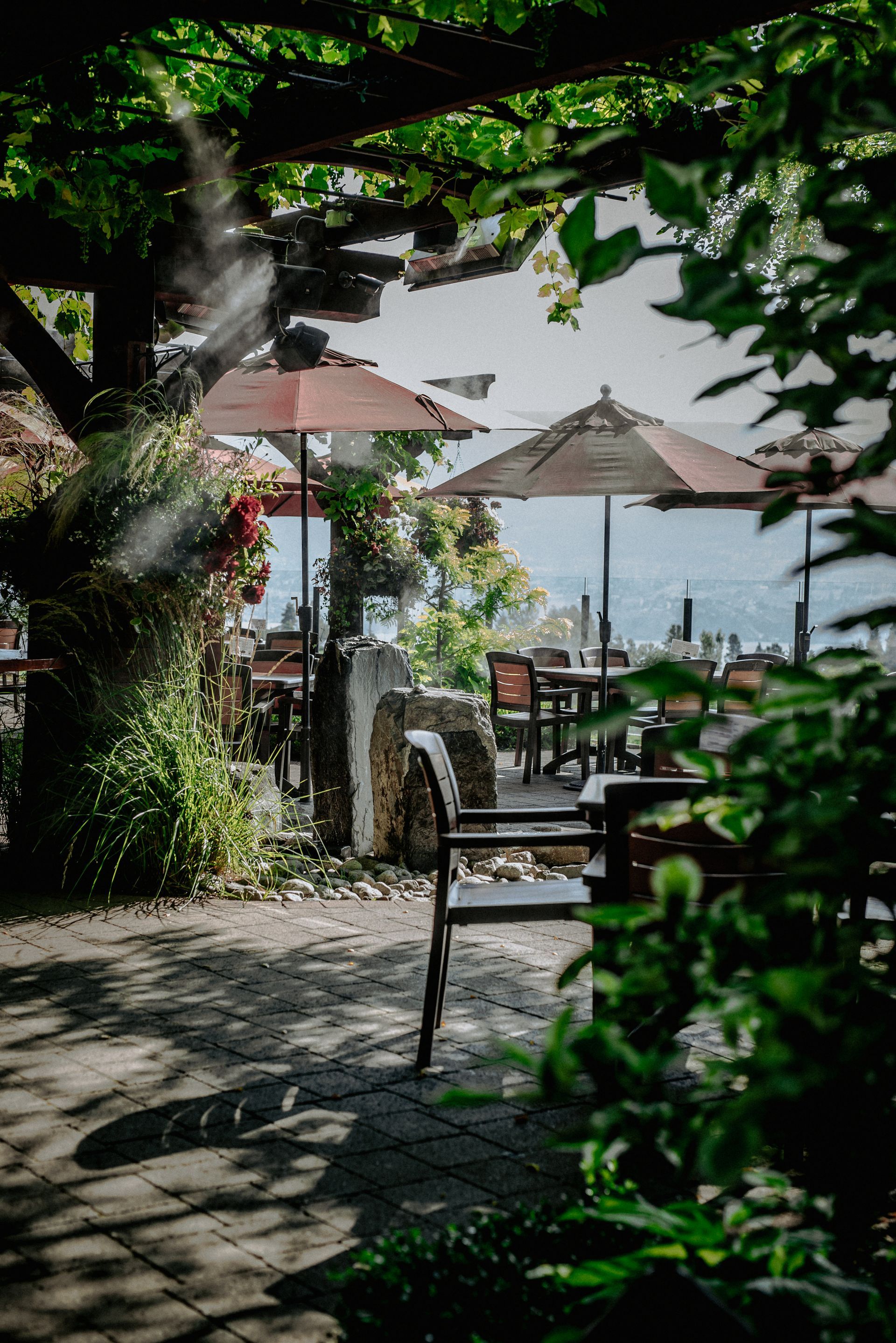 A patio with tables , chairs , umbrellas and a view of the ocean.