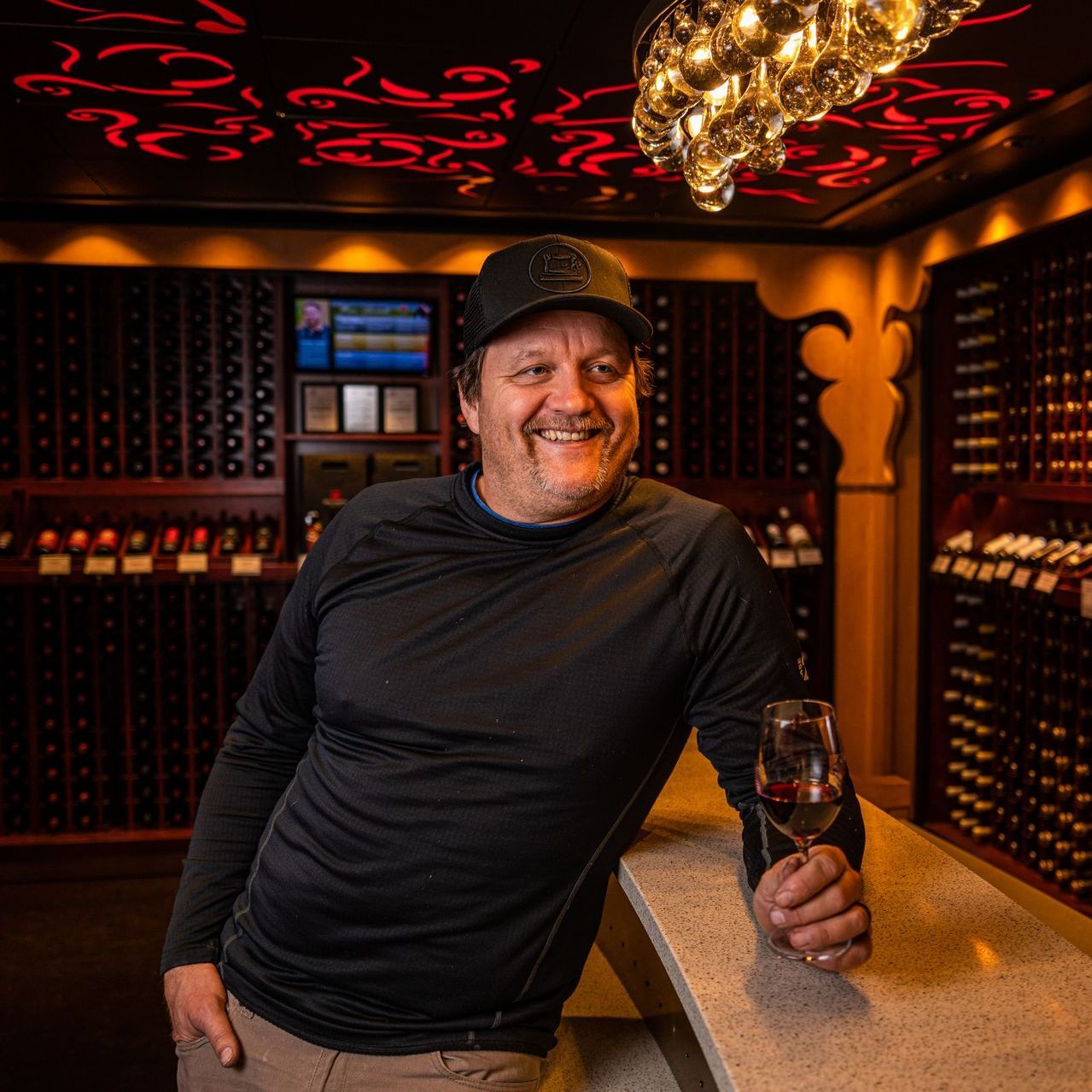 A man leaning on a counter holding a glass of wine