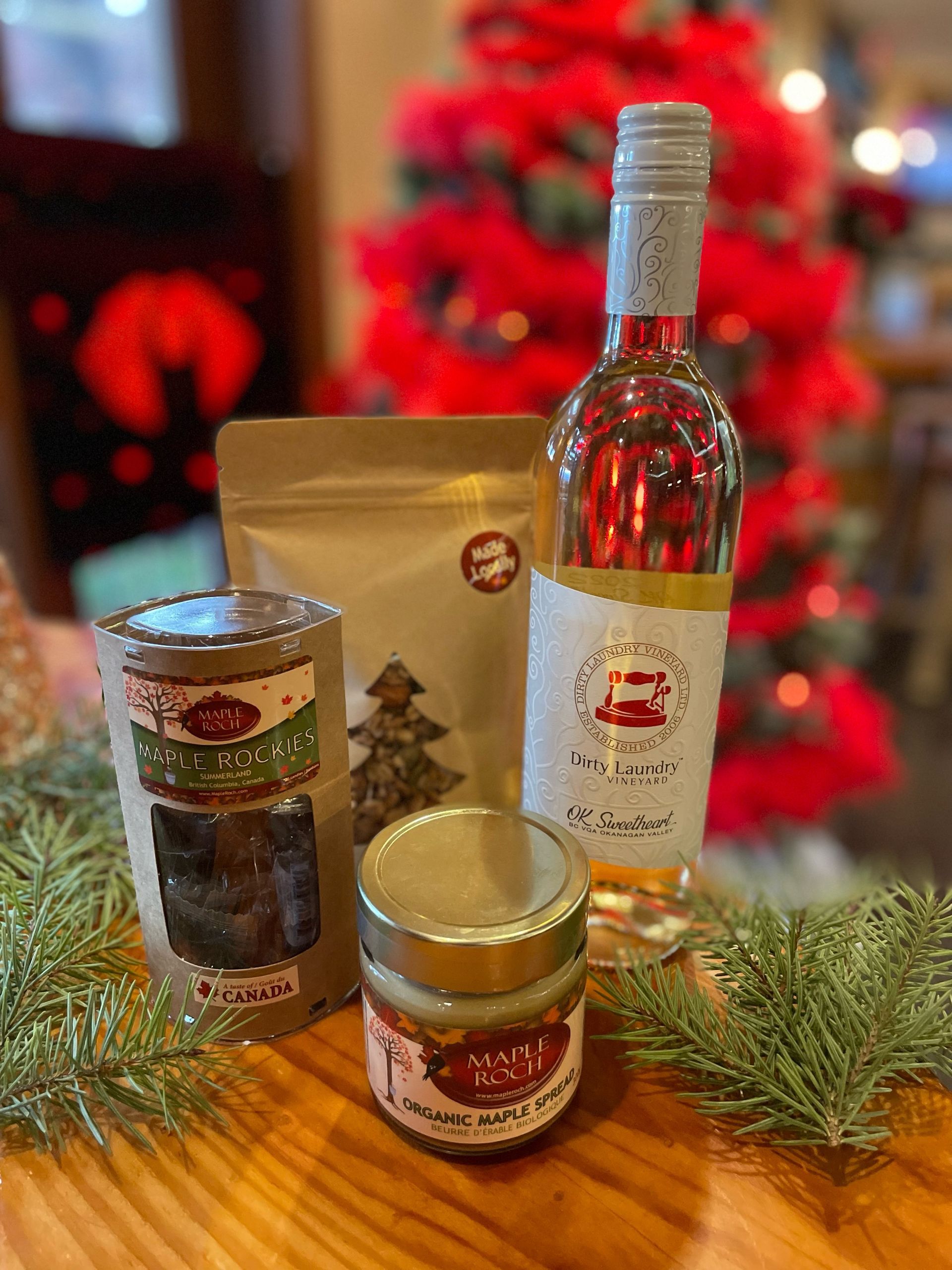 A bottle of wine , jars of food , and a christmas tree are on a wooden table.