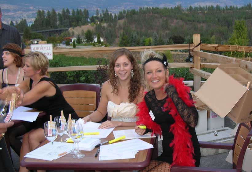 A group of women are sitting at a table with papers and glasses of wine.