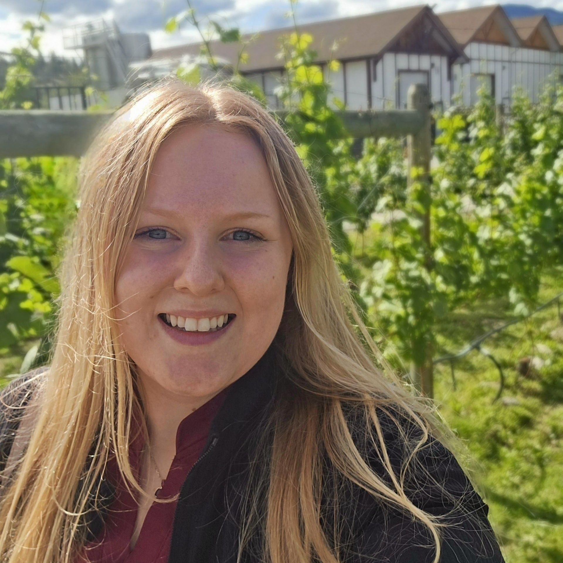 A woman is standing in a vineyard smiling