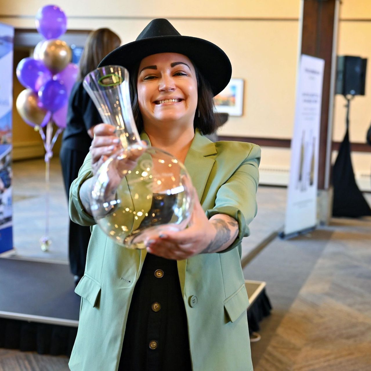 A woman in a green jacket and black hat is holding a glass vase