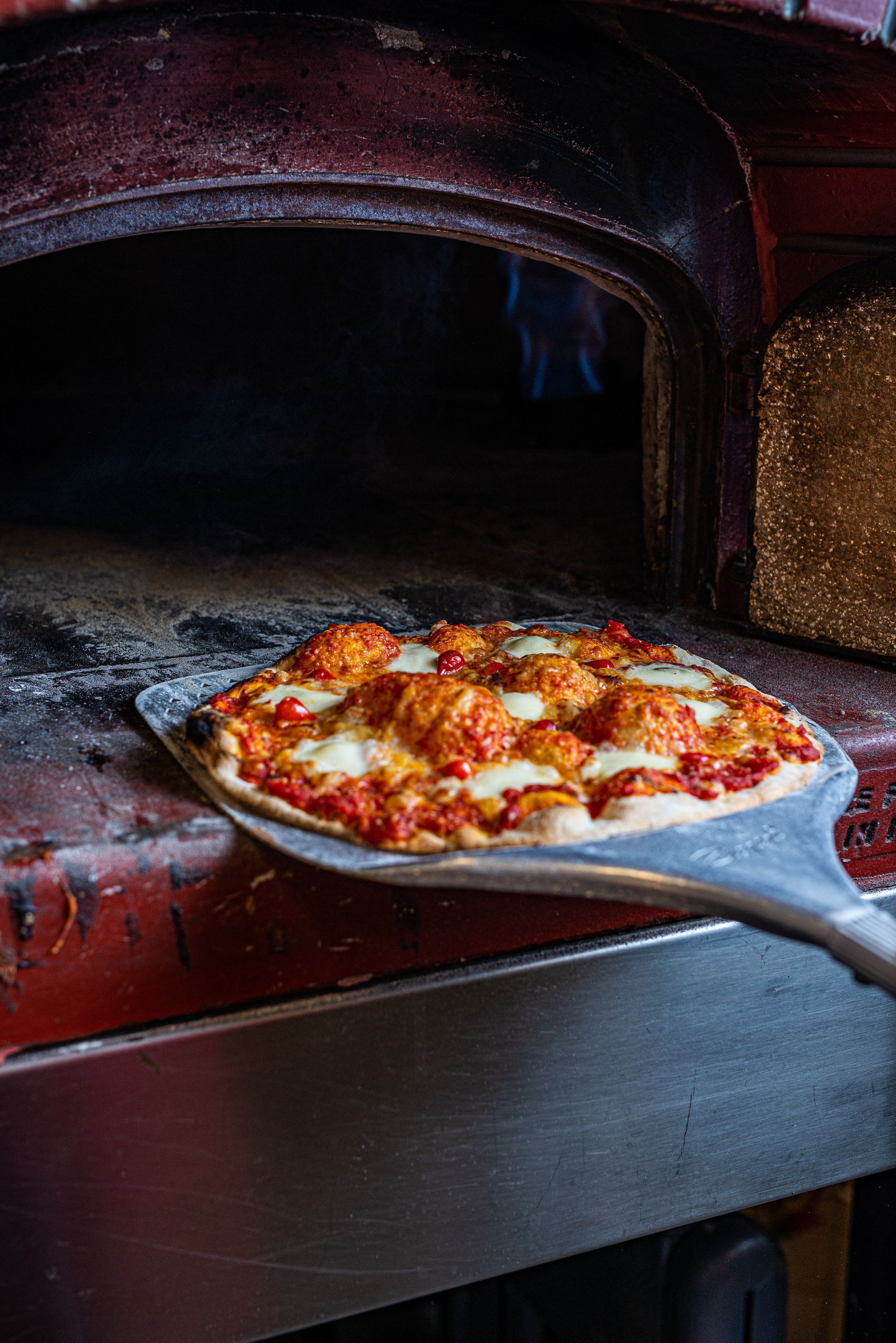 A pizza is being taken out of an oven on a peel.