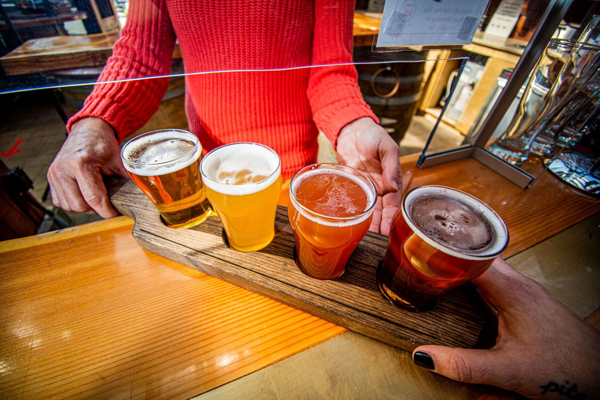 A person is holding a wooden tray with four different types of beer on it.