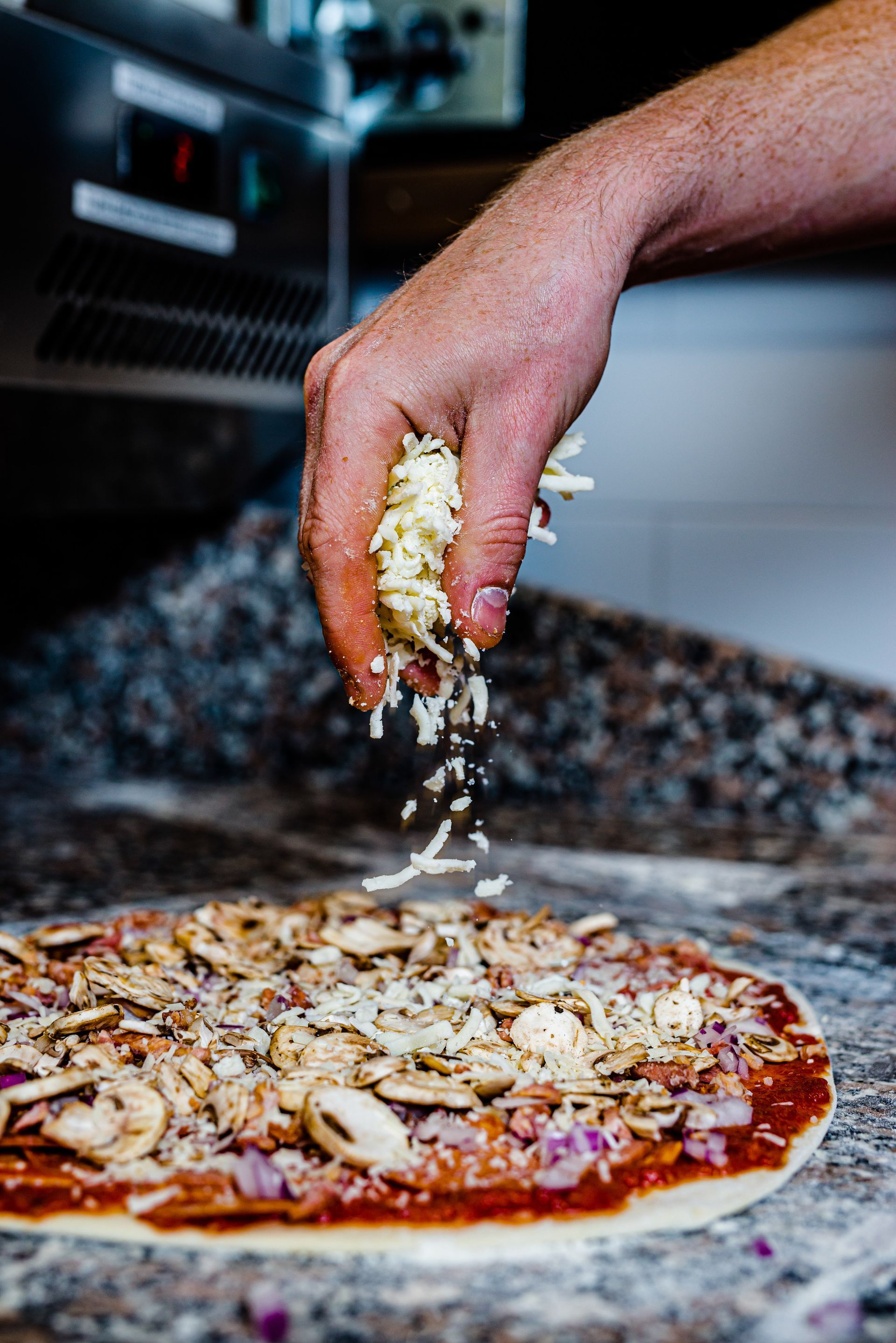 A person is spreading cheese on a pizza on a counter.