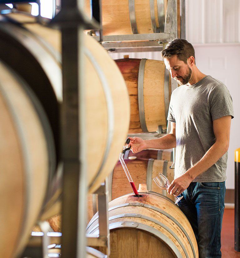 A man is pouring wine into a wooden barrel.