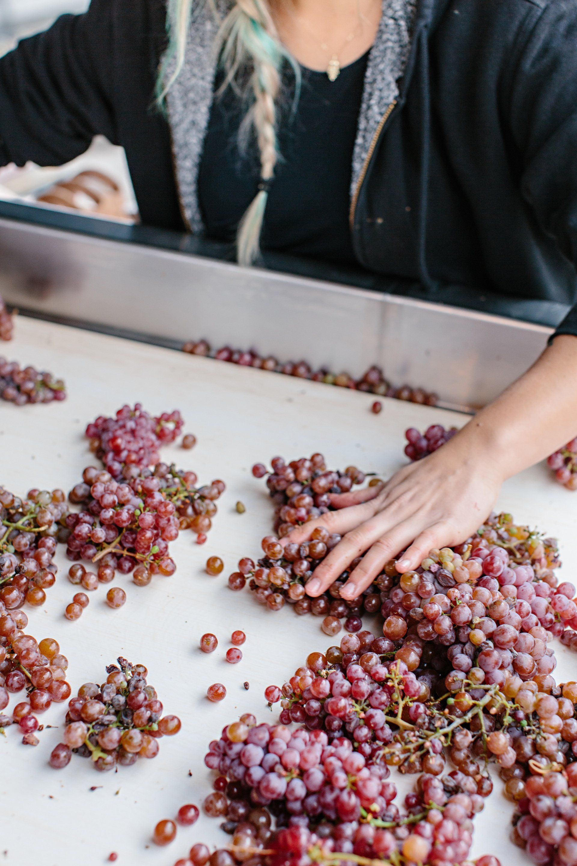 A woman is touching a bunch of grapes on a table.