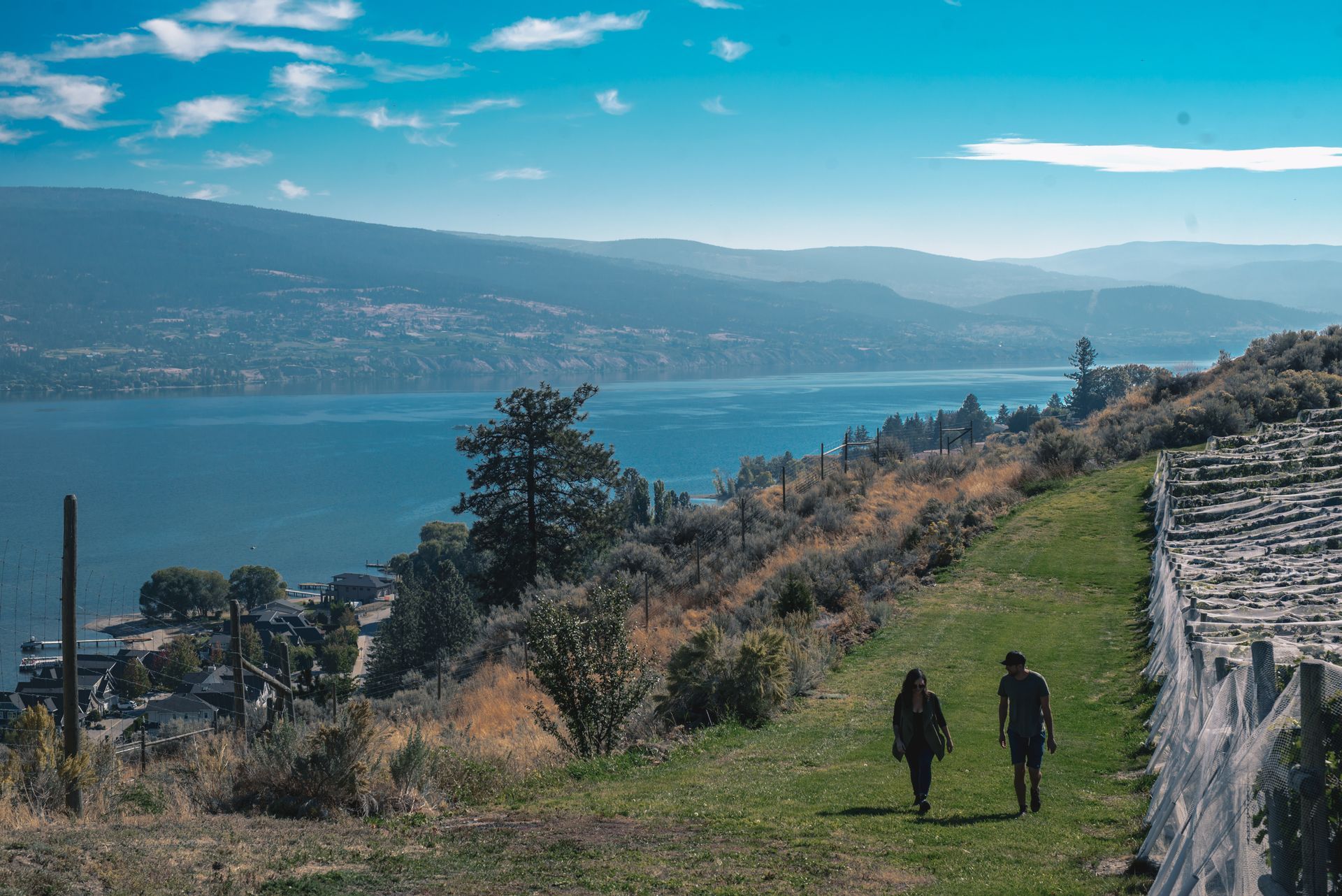Two people are walking on a path next to a lake.