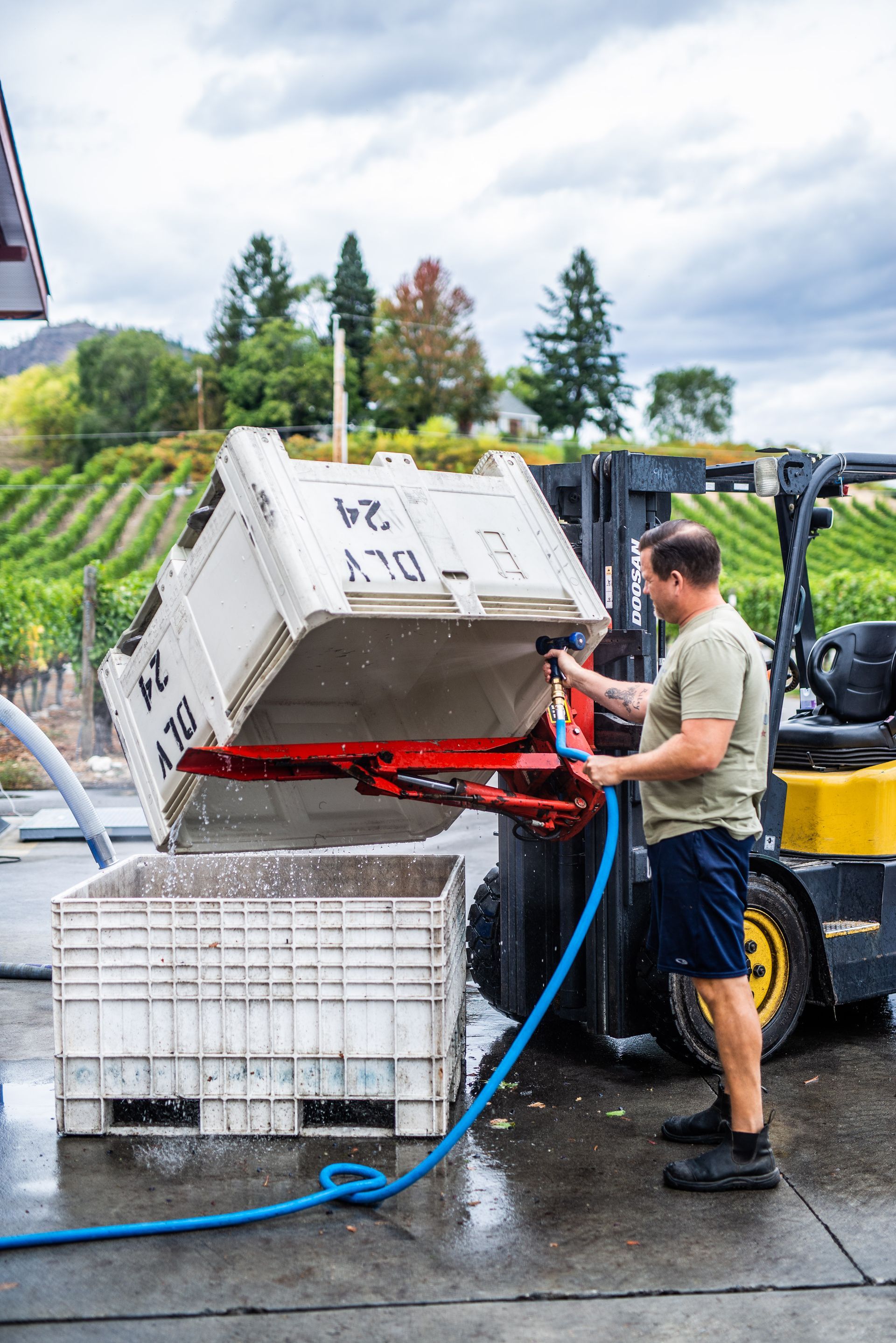 A man is standing next to a forklift with a hose attached to it.