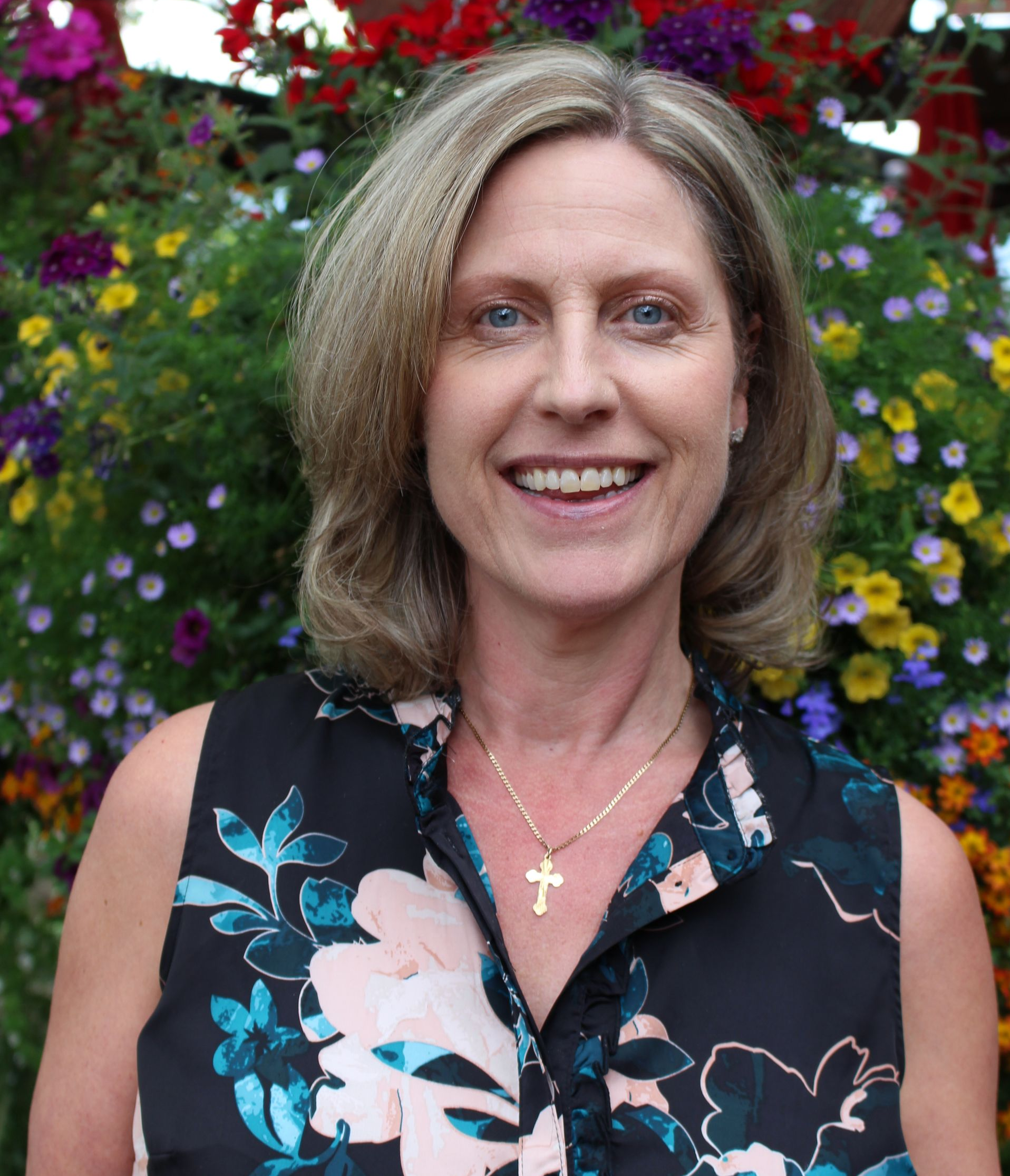 A woman is holding a bottle of wine in front of a wine rack.