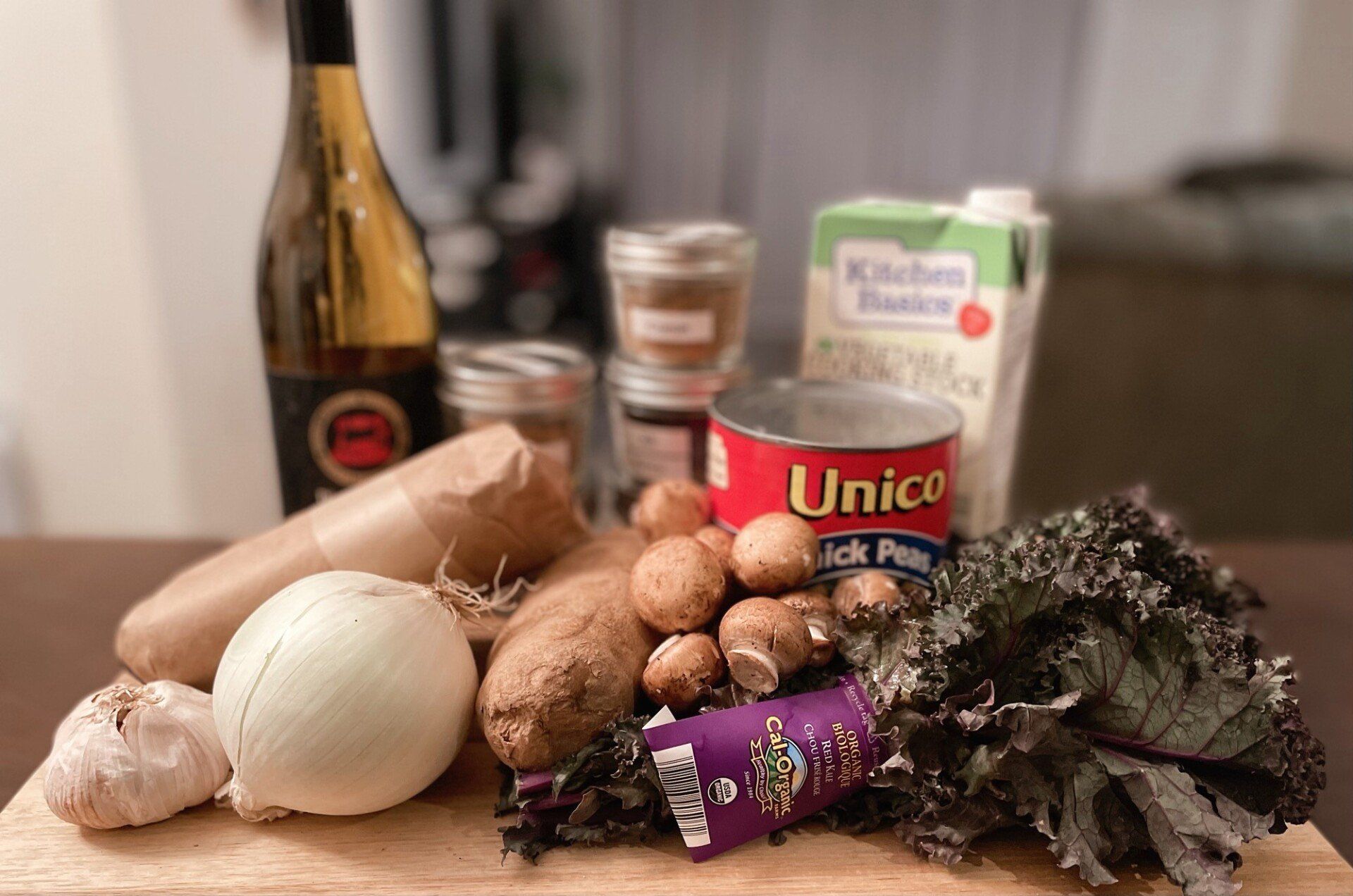 A wooden cutting board topped with vegetables and a bottle of wine.