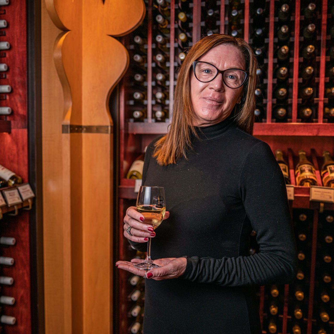 A woman is holding a glass of wine in a wine cellar.