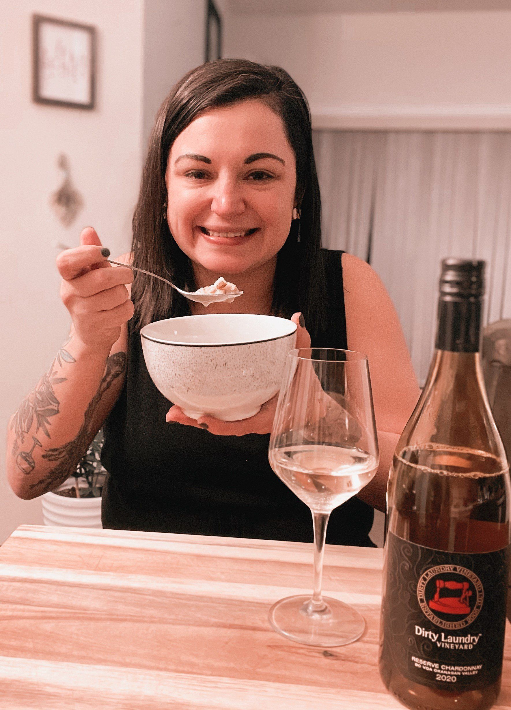 A woman is holding a bowl of food and a glass of wine.