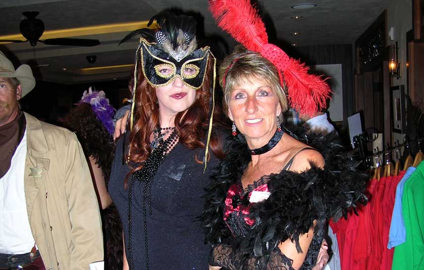 Two women wearing masks and feathers pose for a picture