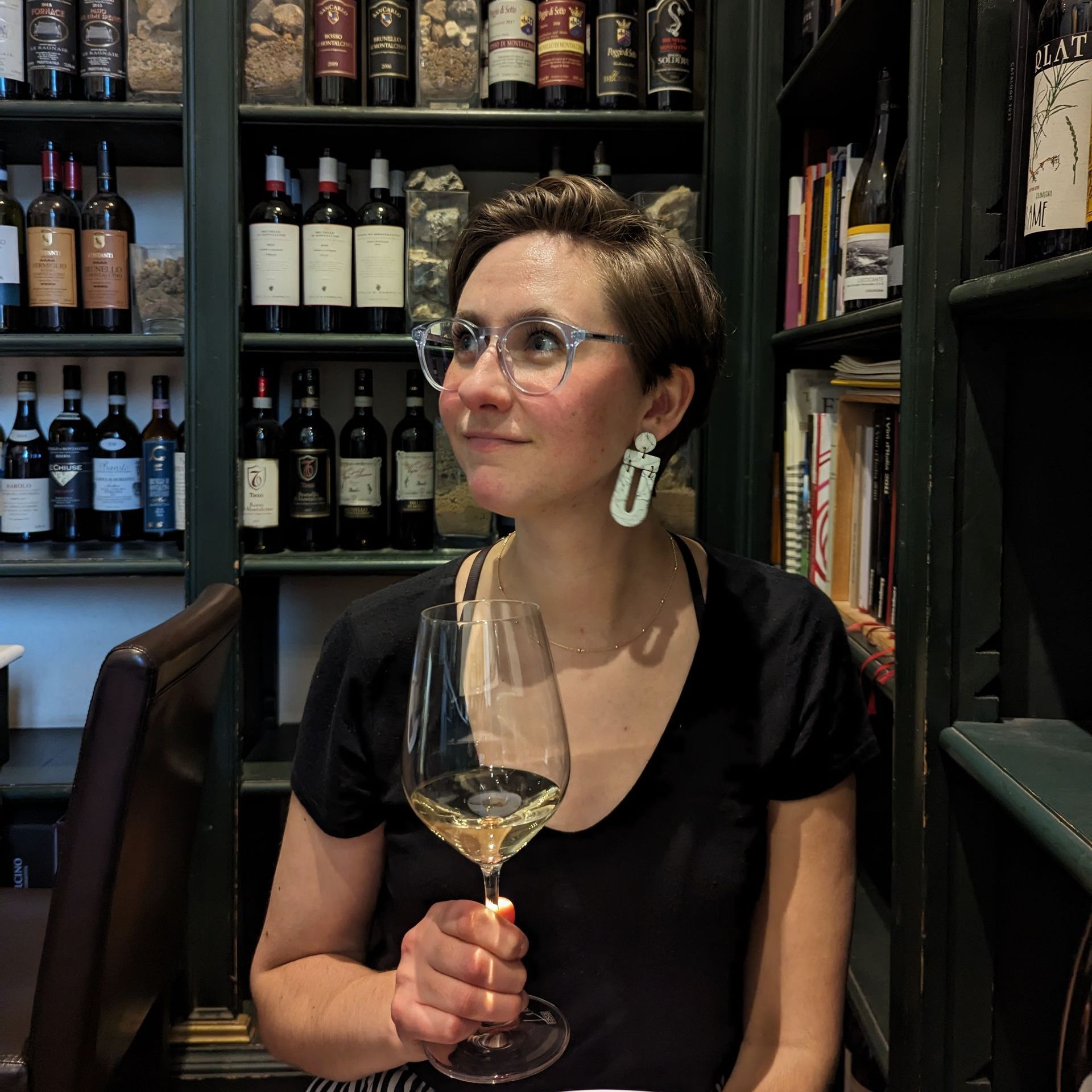 A woman wearing glasses is holding a glass of wine