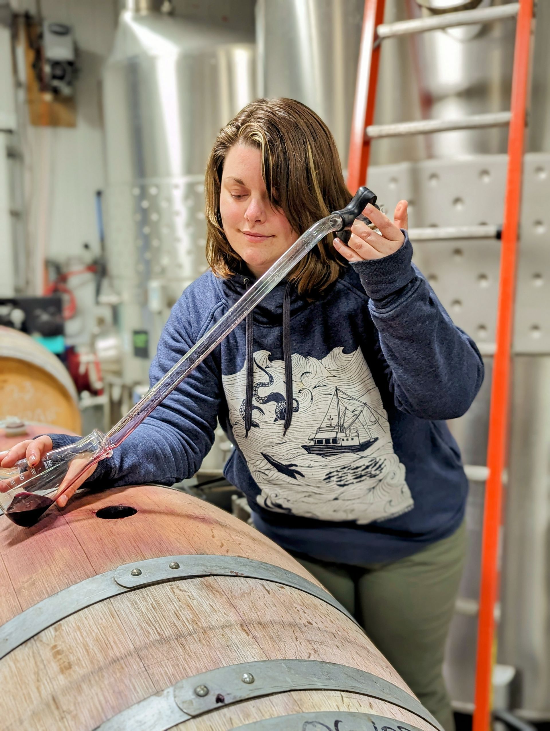 A woman is pouring wine into a wooden barrel.