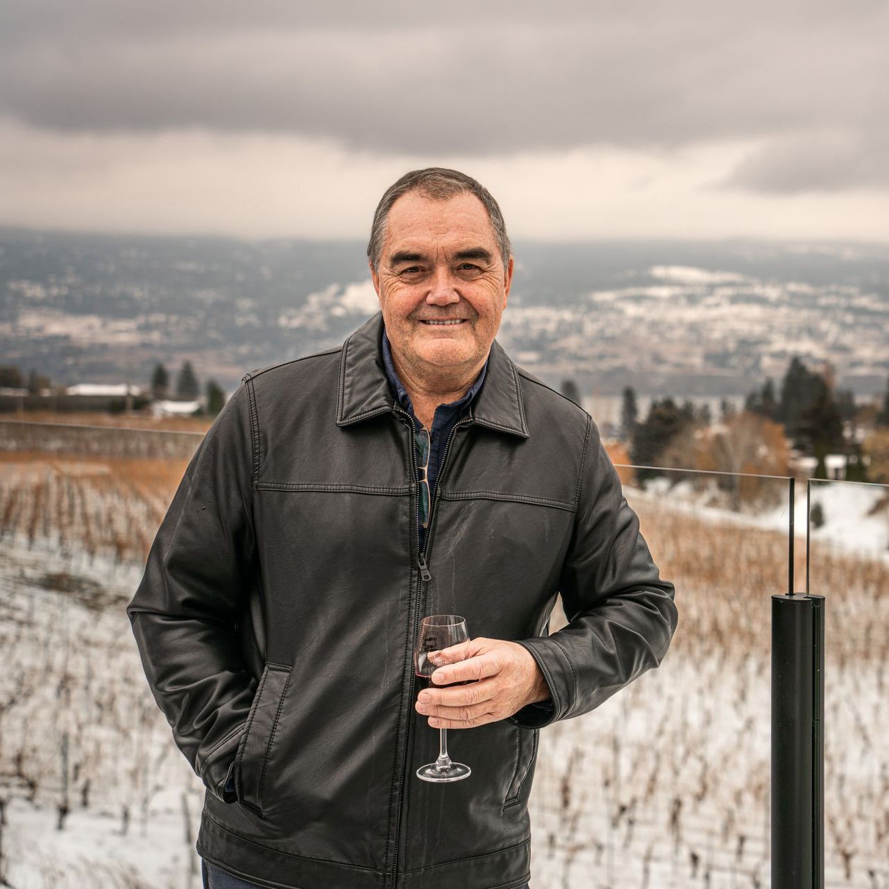 A man in a leather jacket is holding a glass of wine in a snowy field.