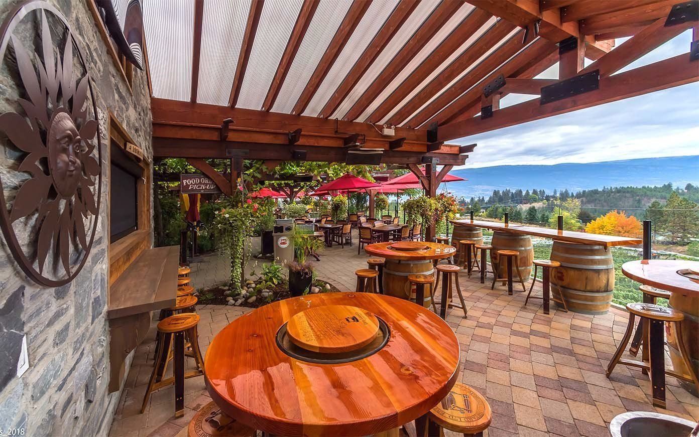 A patio with tables and stools under a pergola with a view of the mountains.