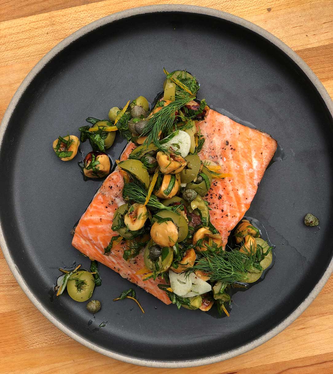 A black plate topped with salmon and vegetables on a wooden table.