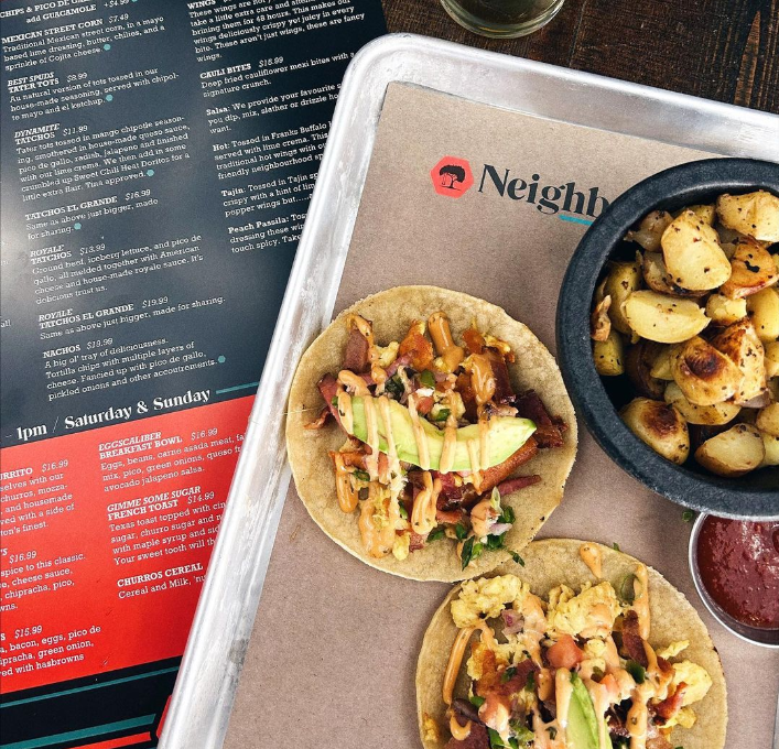 Two tacos next to a bowl of potatoes and a menu