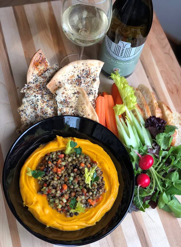 A wooden table topped with a bowl of food and a glass of wine.