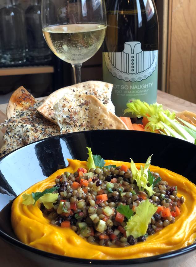 A bowl of food is on a table next to a glass of wine and a bottle of wine.