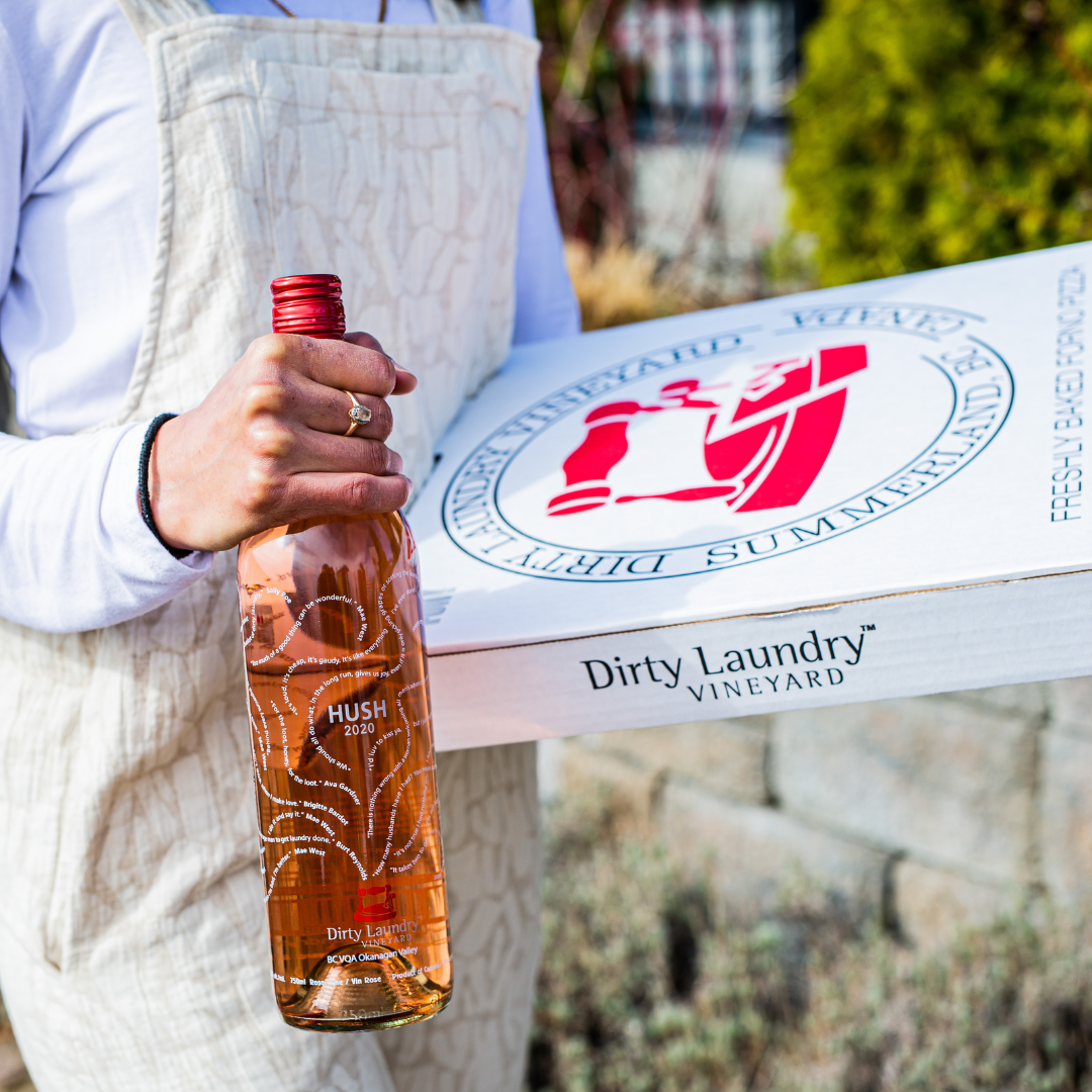A person is holding a bottle of wine in front of a box that says dirty laundry vineyard