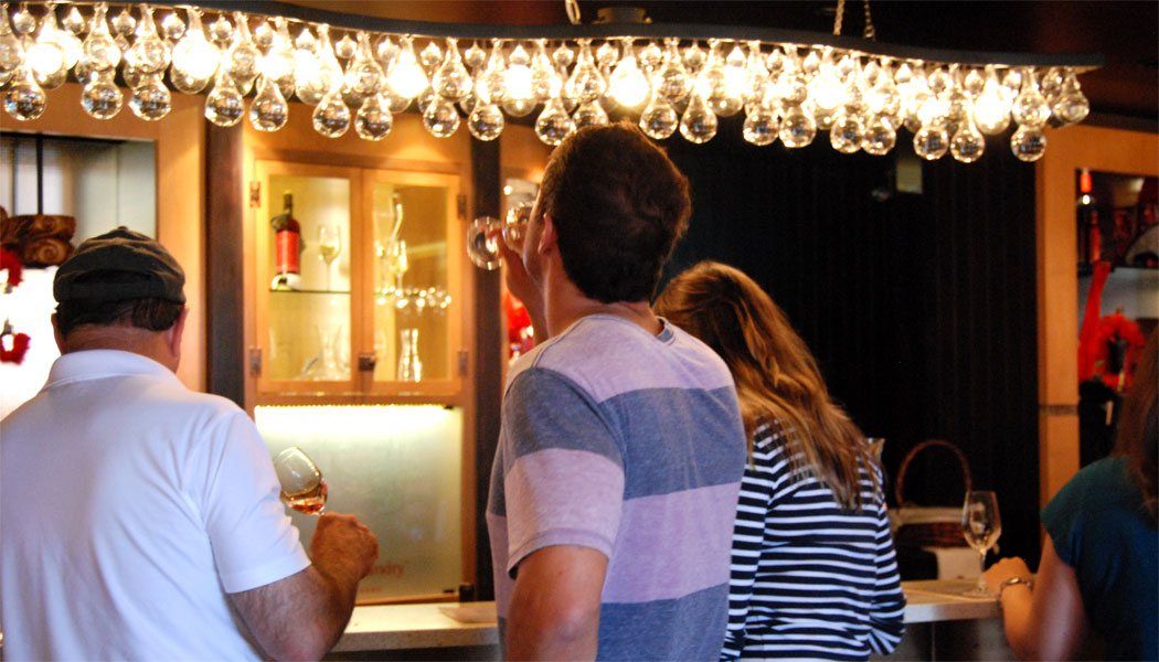 A group of people are standing in a bar looking at wine glasses hanging from the ceiling.