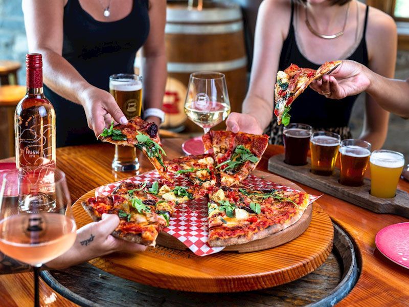 Two women are sitting at a table eating pizza and drinking beer.