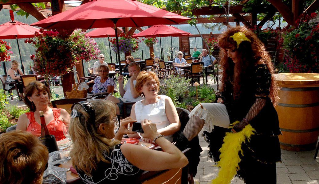 A woman is standing in front of a group of people sitting at tables under red umbrellas.