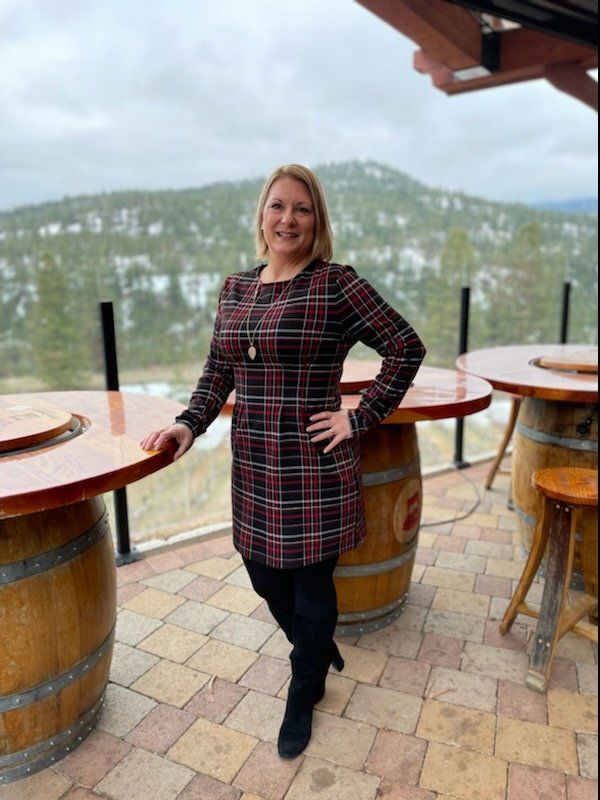A woman in a plaid dress is standing in front of wine barrels.