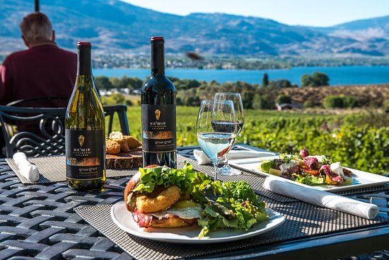 A man is sitting at a table with a plate of food and two bottles of wine.